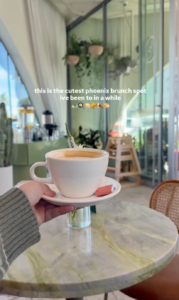 Latte on a marble café table inside a bright, modern coffee shop in Phoenix, Arizona, with hanging plants and floor-to-ceiling windows.