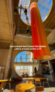 Modern café interior in Arizona featuring soaring ceilings, circular windows, and a large orange hanging art installation overlooking the desert landscape.