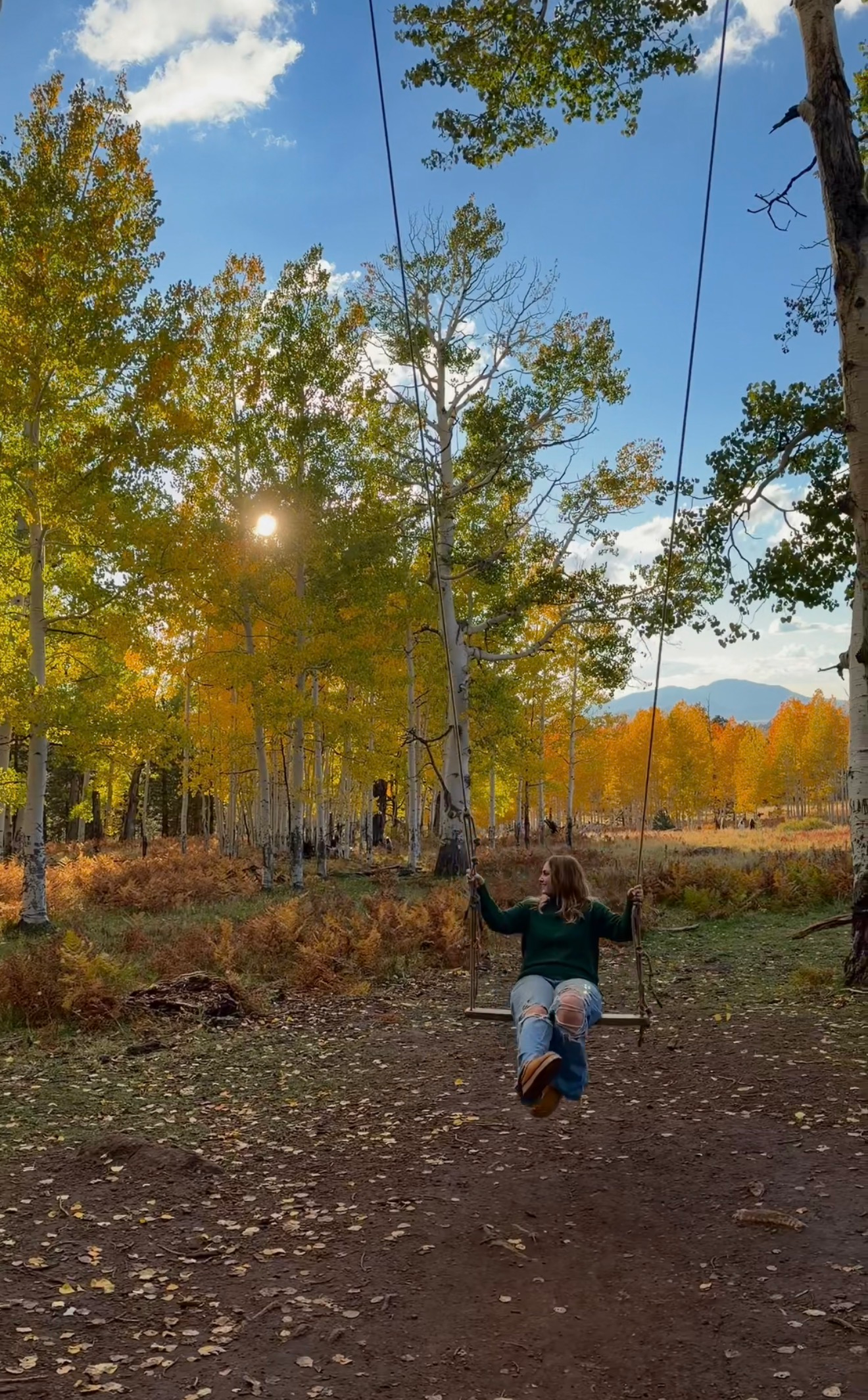 girl in fall outfit on a swing in the forest